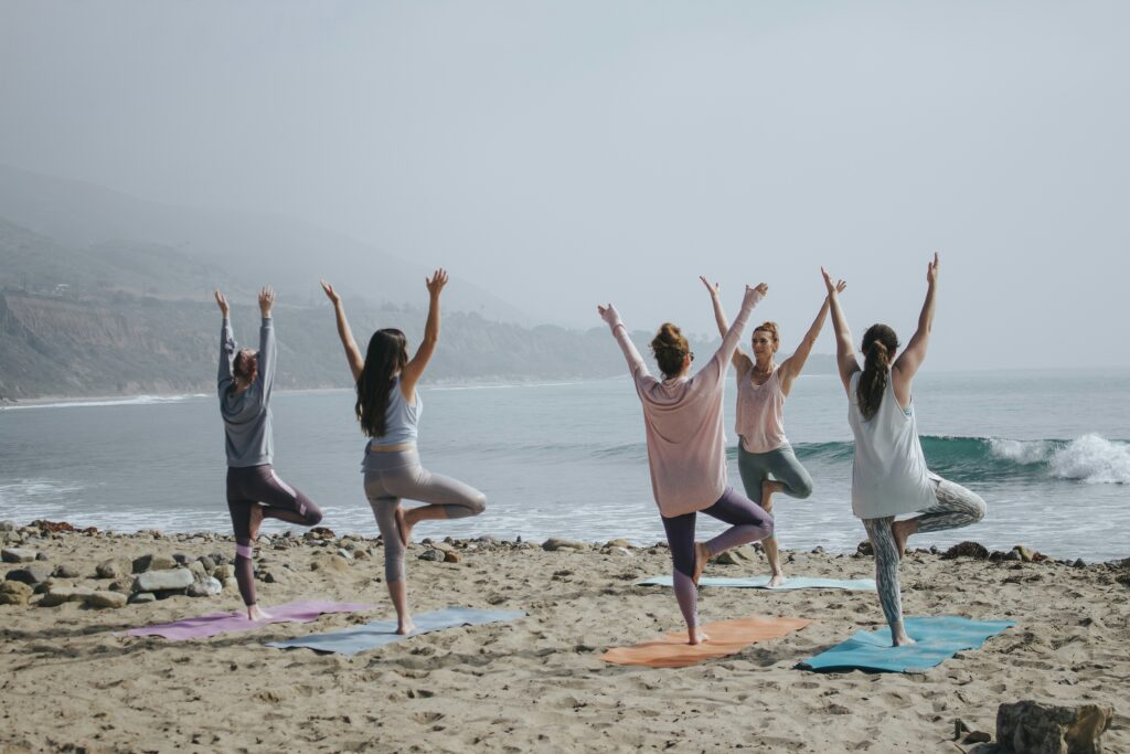 Group practicing Somatic Yoga near a beach, embracing relaxation and wellness through mindful movement.