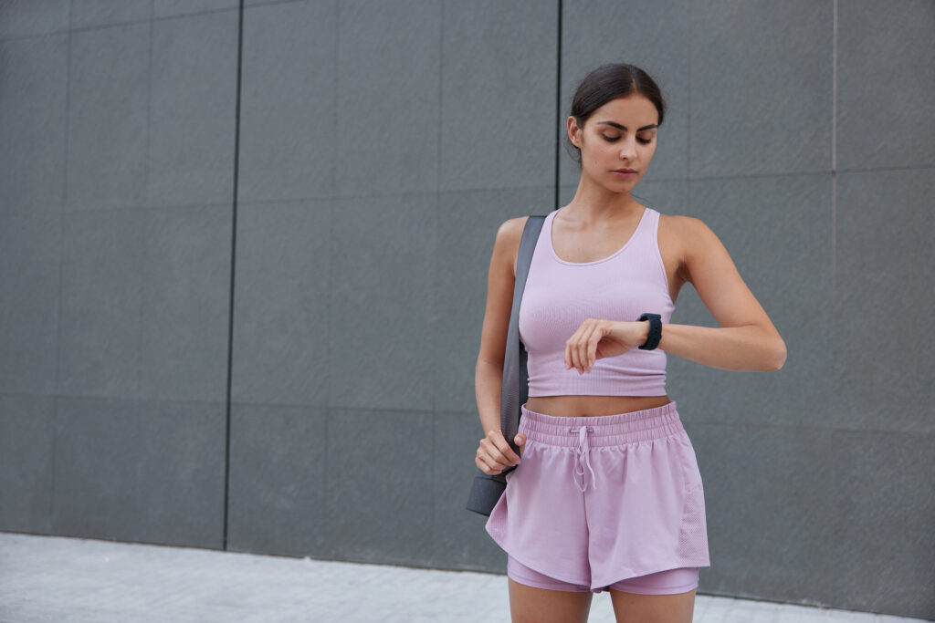 A woman in activewear checks results of fitness training on wearable wristwatch.